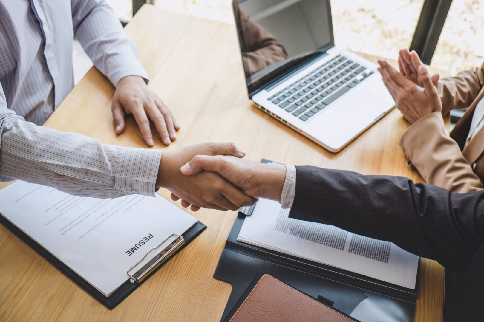 Two people shaking hands over a wooden table.