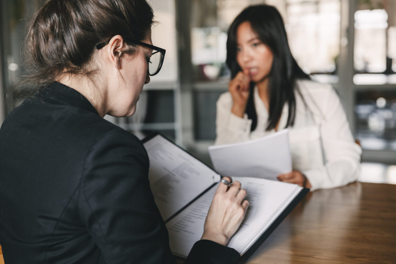 Photo from back of serious businesswoman interviewing and talking with uptight female personnel during job interview - business, career and placement concept