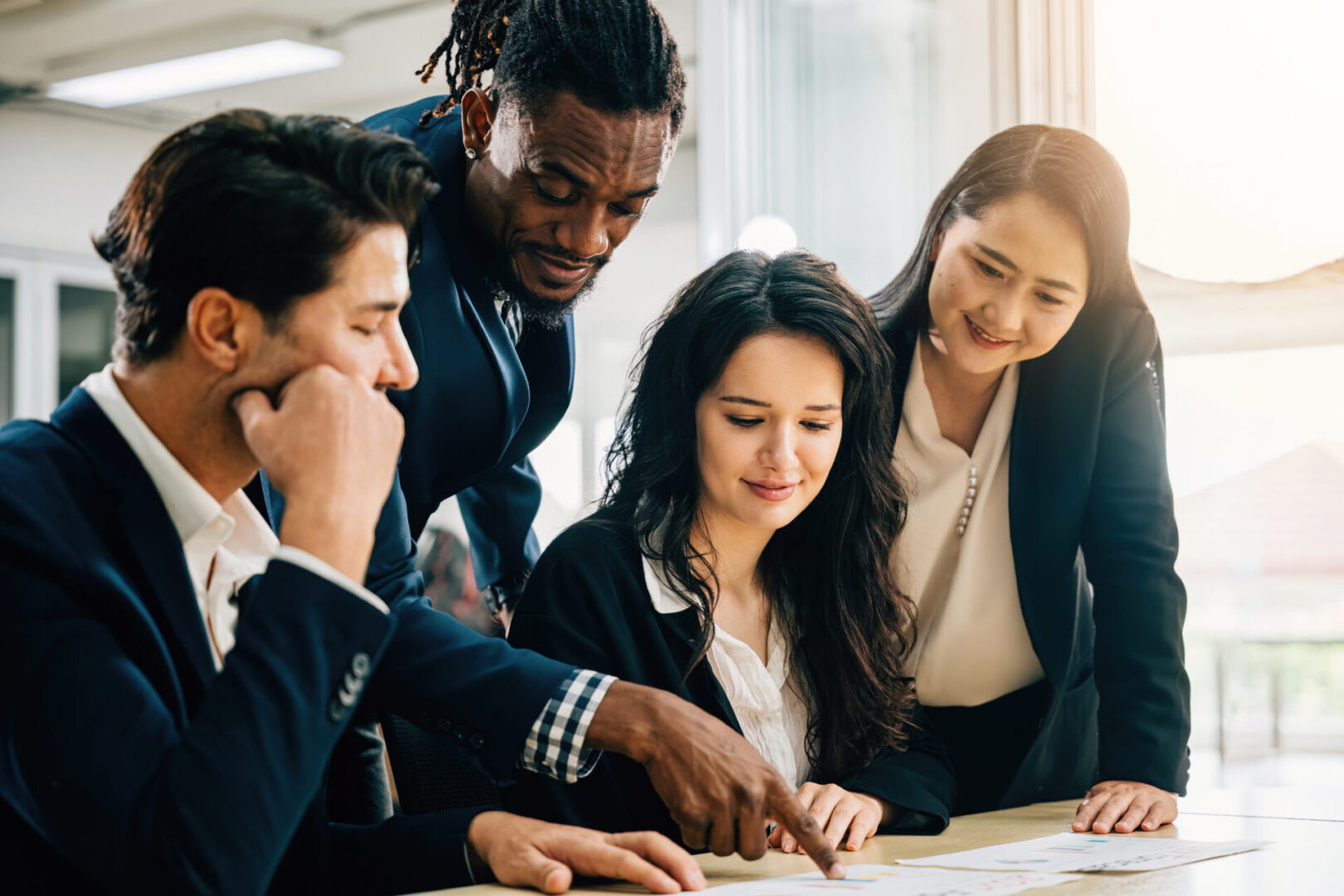 A diverse international business team, led by a female boss, collaborates at a meeting table. Together, they discuss financial results, review paperwork, and share ideas for success. Teamwork