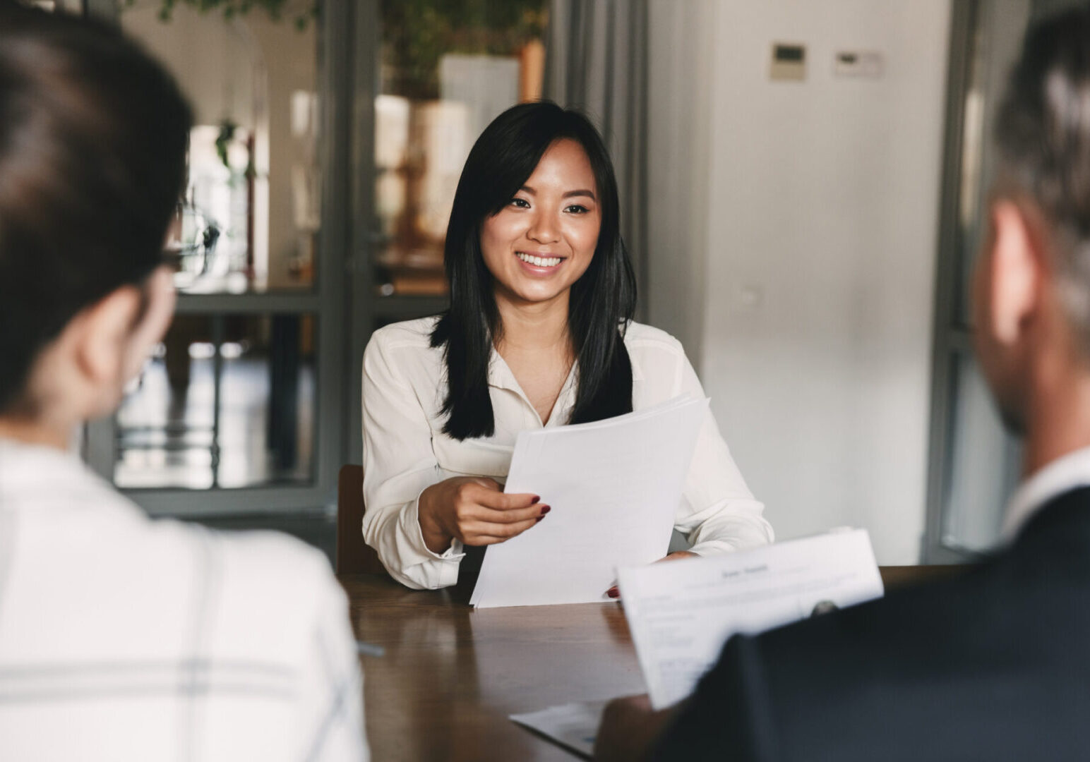 Business, career and recruitment concept - young asian woman smiling and holding resume while interviewing as candidate for job in big company