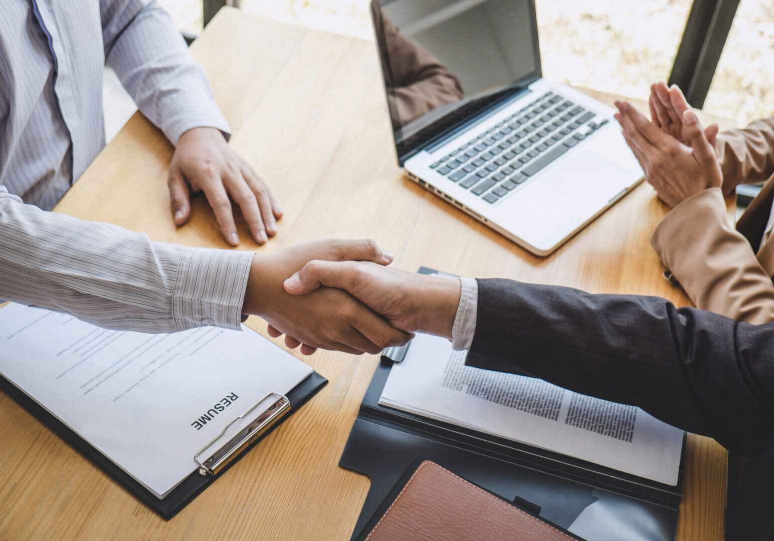 Two people shaking hands over a wooden table.