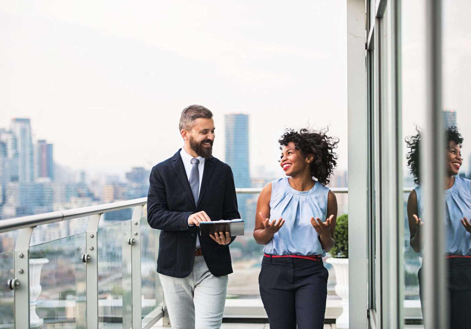 Two people are walking on a balcony with one holding a tablet.